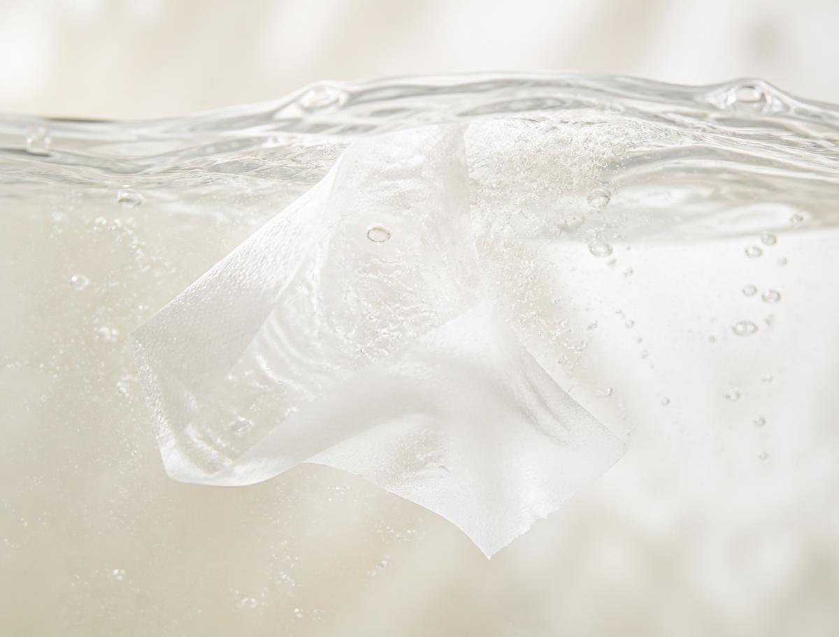 A thin white detergent sheet dissolving in clear water